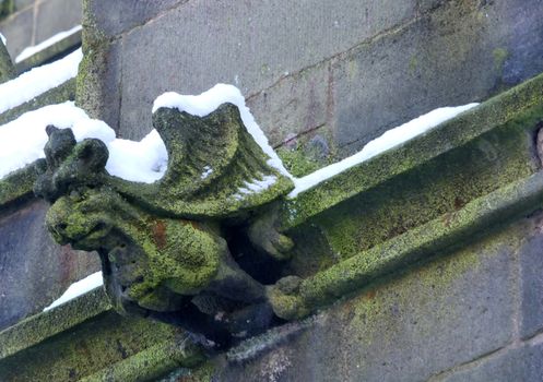 a dragon like grotesque on the wall of an old church in heptonstall with wings and a lion like face covered in snow and moss