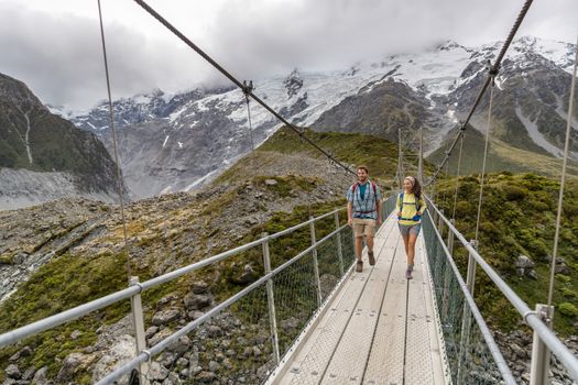 Hooker Valley Track hiking trail, New Zealand. Hikers people crossing bridge on the Hooker Valley track, Aoraki, Mt Cook National Park with snow capped mountains landscape