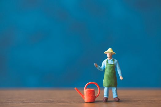 Miniature people gardener standing in front of a blue wall backg