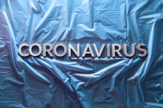 the word coronavirus laid with silver letters on crumpled blue plastic film - flat lay with centered composition