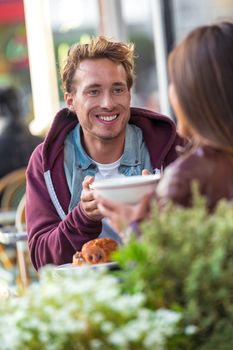 Man talking with girlfriend at cafe table. Friends meeting in city having fun drinking coffee. Couple on a date, young people having brunch at restaurant, city lifestyle.
