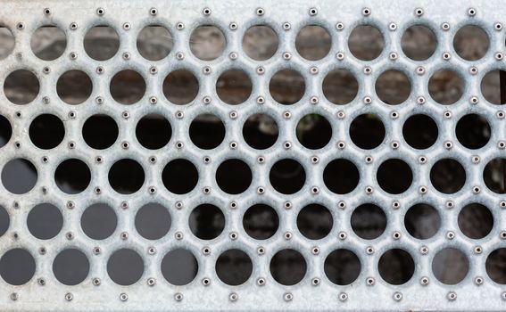 Metal grate with round holes and rivets.