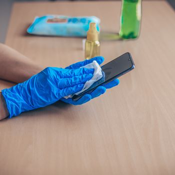 Woman's hand in blue gloves sanitizing cleaning smartphone mobil