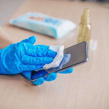 Woman's hand in blue gloves sanitizing cleaning smartphone mobil
