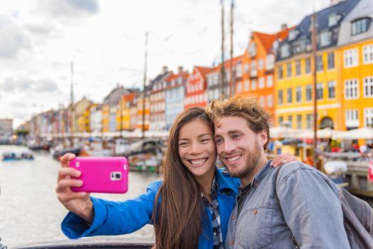 Copenhagen travel couple tourists taking selfie photo with phone camera. Smiling young people students at old port Nyhavn, tourism danish landmark in Denmark, northern Europe.