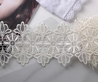 Tapes of ecru white guipure, beauty silk lace fabric on light background.