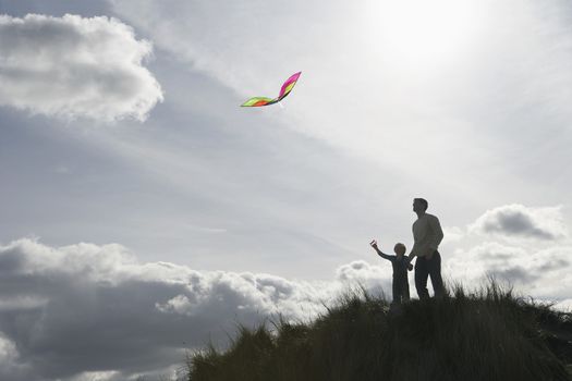 Silhouette of girl and father flying kite on dunes