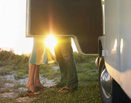 Young couple face to face beside camper van low section