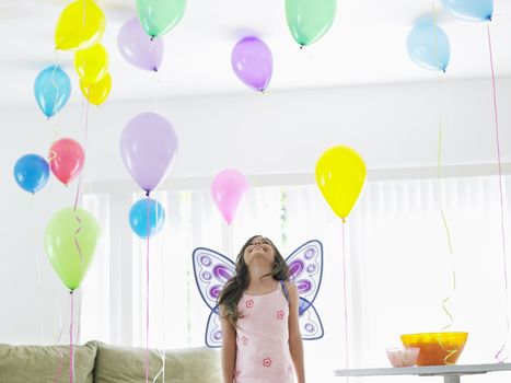 Young girl (7-9) with fairy wings in room full of balloons