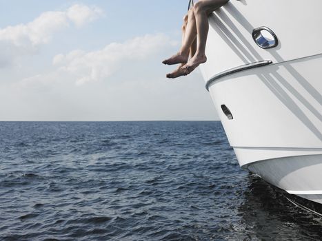 Low angle view of couple's legs with bare feet dangling over the side of a yacht