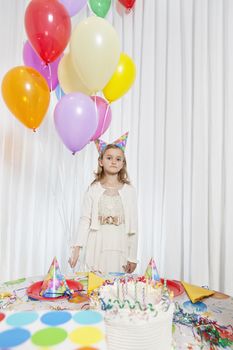 Portrait of a young girl holding party balloons with cake on table