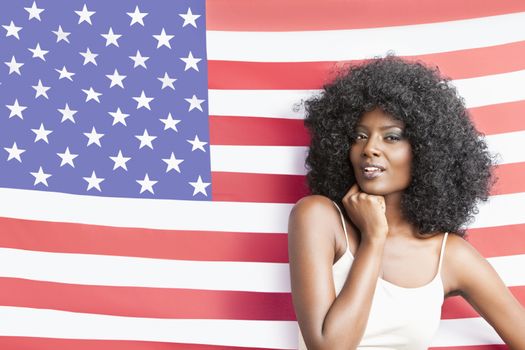 Portrait of stylish young woman with fizzy hairstyle standing against American flag