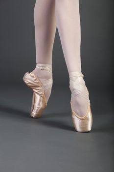 Low section of young female ballet dancer with legs crossed tiptoeing over grey background