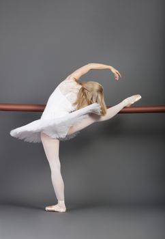 Young female ballet dancer stretching at ballet bar over grey background