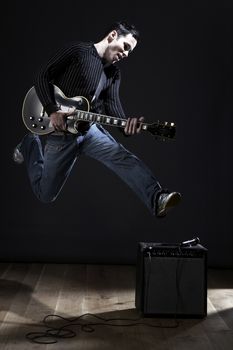 Young man with electric guitar jumping on stage