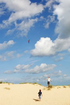 Father and Son Flying Kite on sand dune on beach