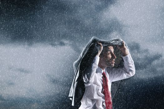 Businessman covering head with jacket during rainstorm