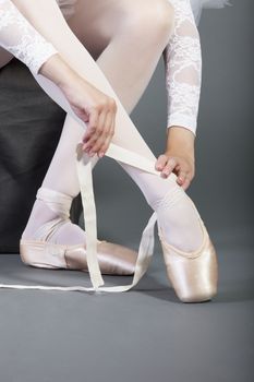 Low section of female ballet dancer tying pointe shoes