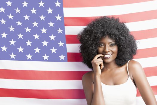 Portrait of young woman with fizzy hairstyle standing against American flag