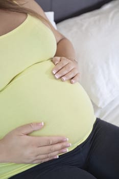 Midsection of young pregnant woman with hands on stomach relaxing at home