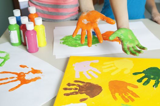Close-up of paint covered hands and colorful handprints on papers
