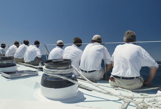 Sailing crew sitting on side of yacht on ocean back view