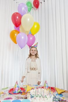Portrait of a happy girl holding party balloons with cake on table