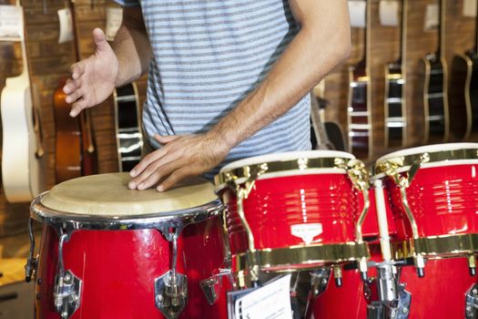 Midsection of a man playing bongo drums in music store