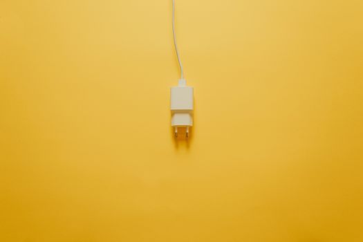 A white charger with a cable over a yellow table
