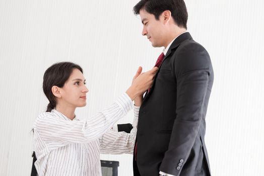 Wife tying red necktie to her husband in the office with smiling