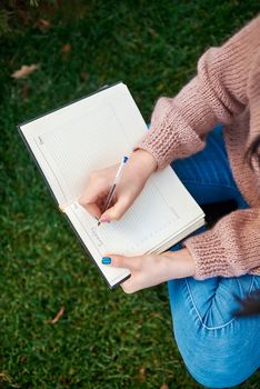 Female hands holding pen and paper diary on blurred grass background