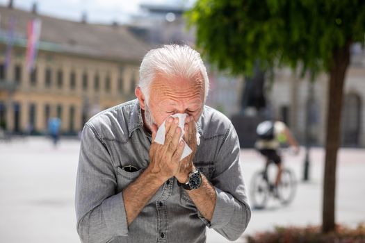 Old man man coughs and sneezes into a handkerchief on street, al