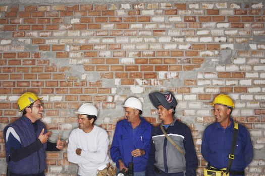 Group of laughing construction workers by brick wall