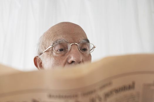 Senior man in spectacles reading newspaper close up