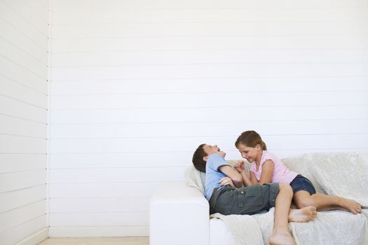 Young girl tickling young boy on couch in weather boarded room