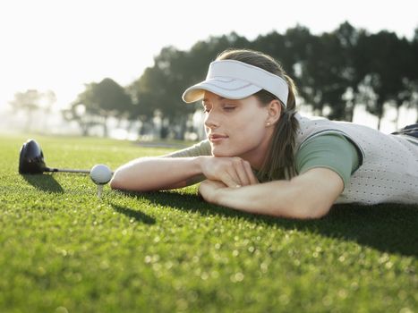 Young female golfer lying on court looking at ball on tee