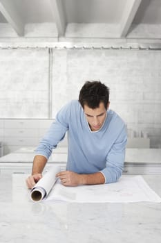Young man leaning on table looking at blueprint