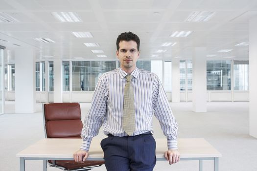 Office worker perching on edge of table in empty office space