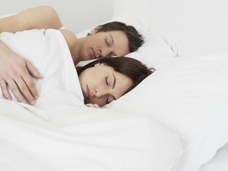 Young couple sleeping in bed man's arm around woman