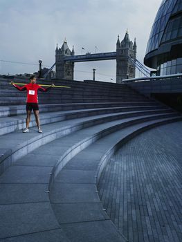 Man holding javelin on shoulders standing on steps of The Scoop amphitheatre London England