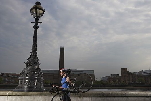 Cyclist carrying bicycle along river embankment side view London England