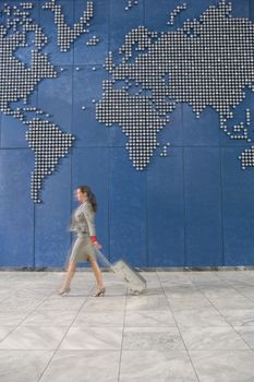 Woman with suitcase walking past world map on wall