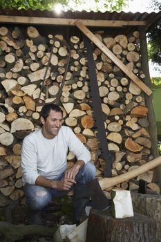 Man crouching beside axe at timber shed