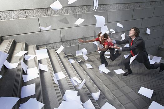 Busines man and woman catching falling paperwork on steps