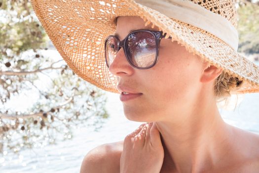 Close up portrait of no makeup natural beautiful sensual woman wearing straw sun hat on the beach in shade of a pine tree