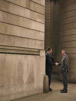 Two businessmen shaking hands at entrance of monumental building