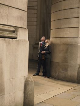 Businessman and businesswoman standing at entrance to monumental building looking up
