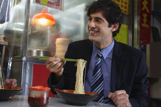 Young business man eating noodles in bar