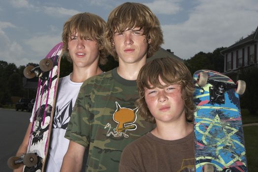 Three teenage brothers (13-17) standing on street holding skateboards portrait