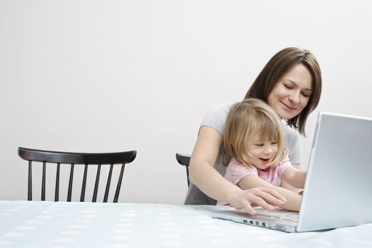 Woman working from home with laptop on table while baby sitting her daughter